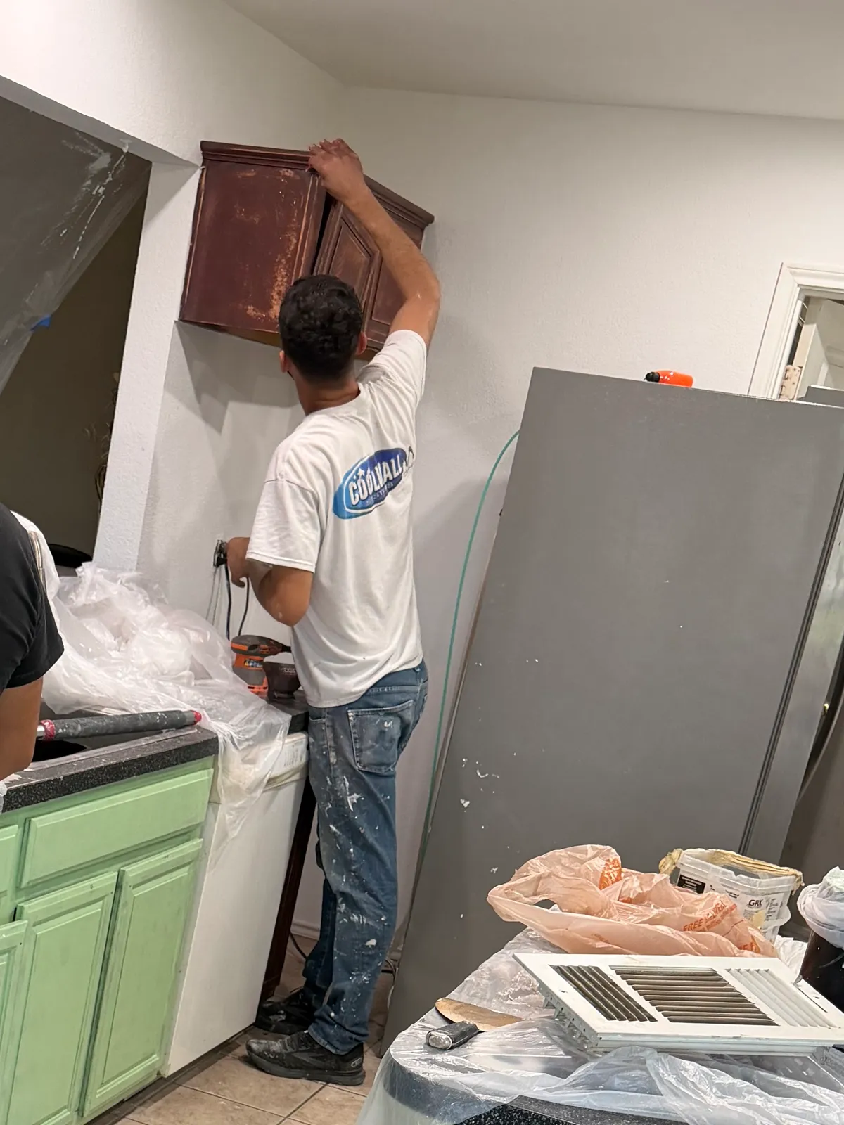 An RGS General Contracting painter removing a dark cabinet door during a kitchen cabinet repaint in the Dallas-Fort Worth area